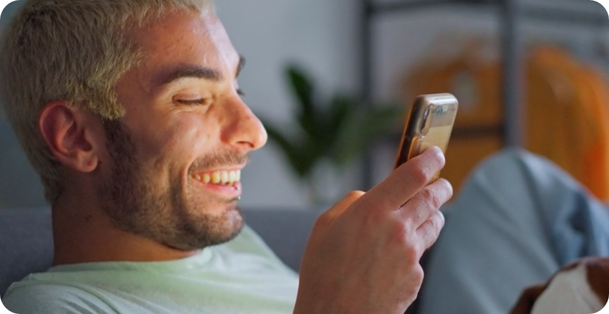 Man sitting on a couch looking at his phone with a joyous smile.