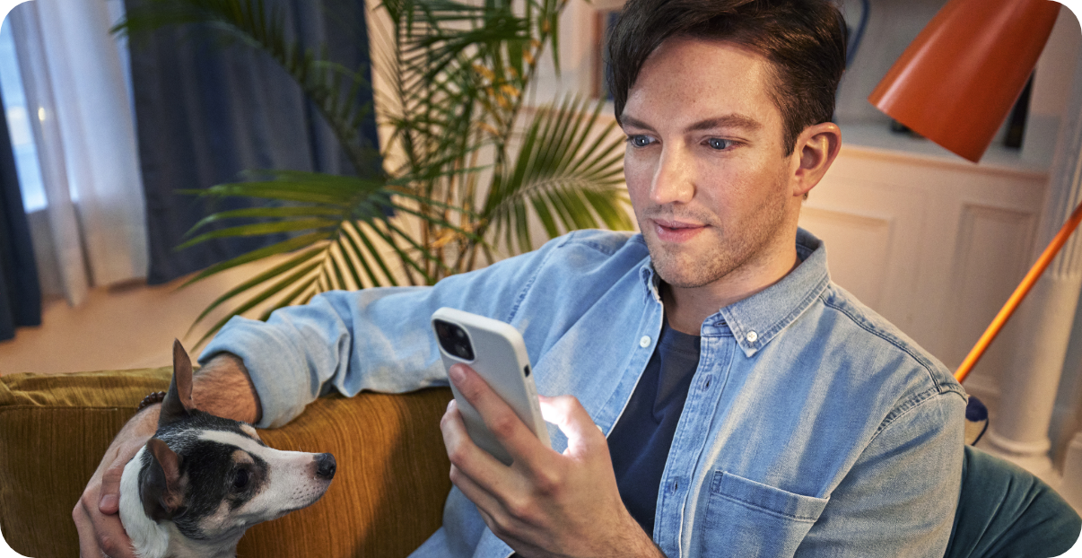 Man sitting on a couch looking at his phone with a joyous smile.