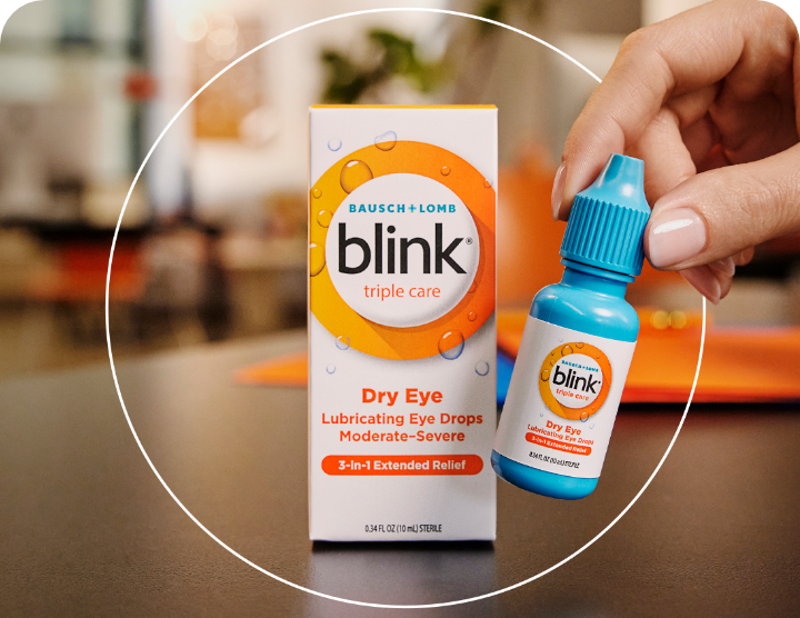 Blink Triple Care Lubricating Eye Drops package on a table with an individual bottle being picked by a hand