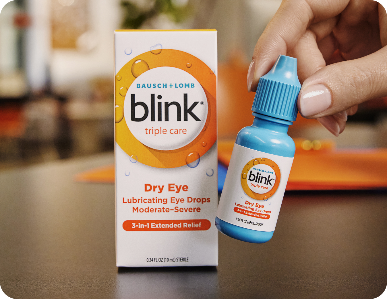 Blink Triple Care Lubricating Eye Drops bottle and carton on a desk in front of a computer monitor